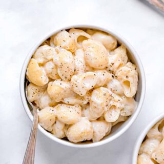 shelled pasta covered in creamy sauce in a white bowl