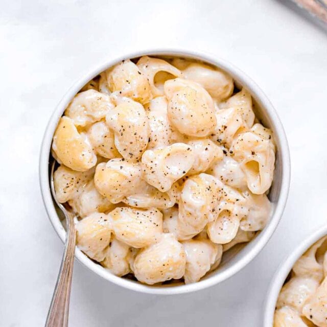 shelled pasta covered in creamy sauce in a white bowl