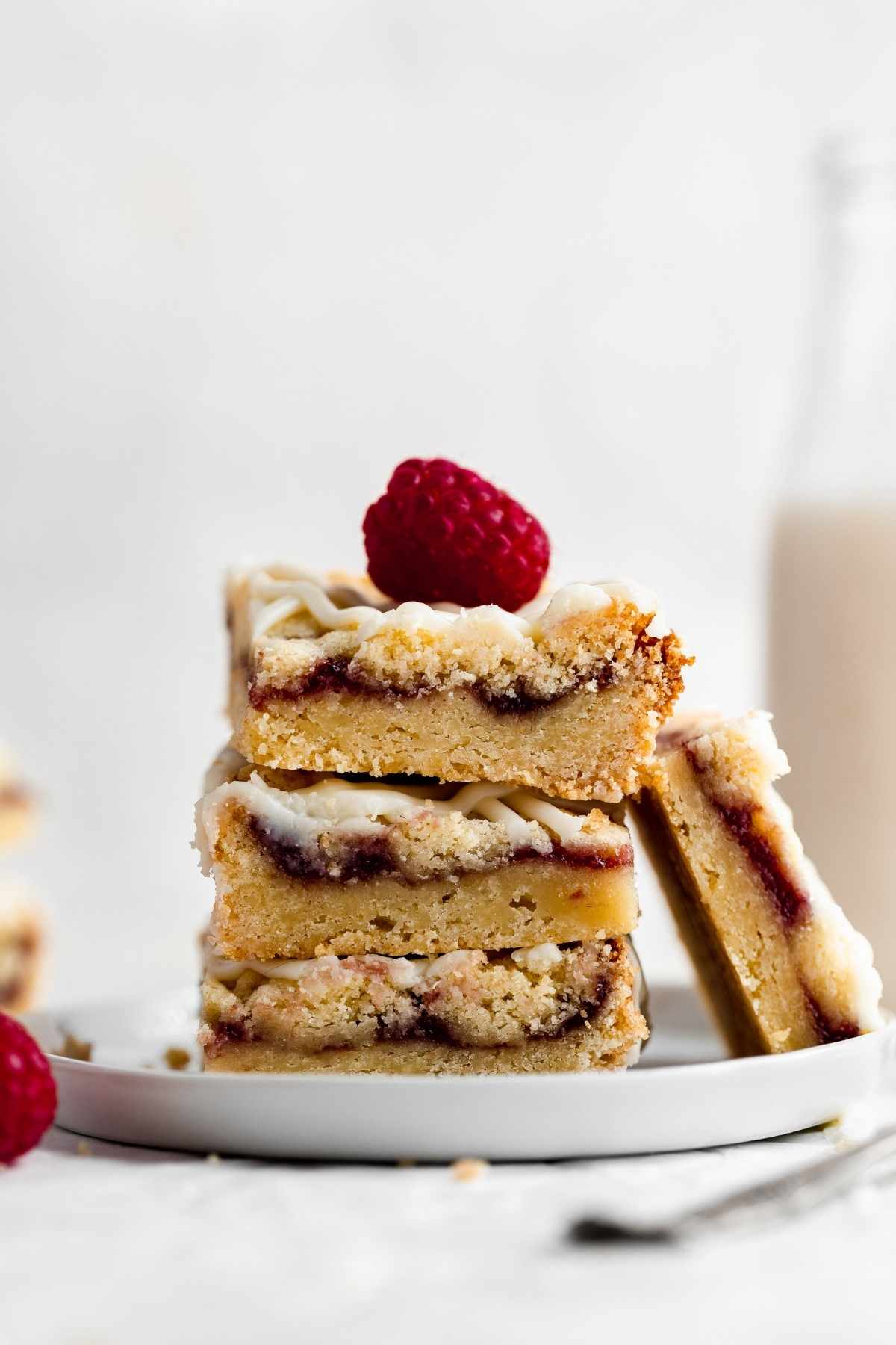 White Chocolate Raspberry Shortbread Bars sliced and stacked on a plate with fresh raspberry garnish
