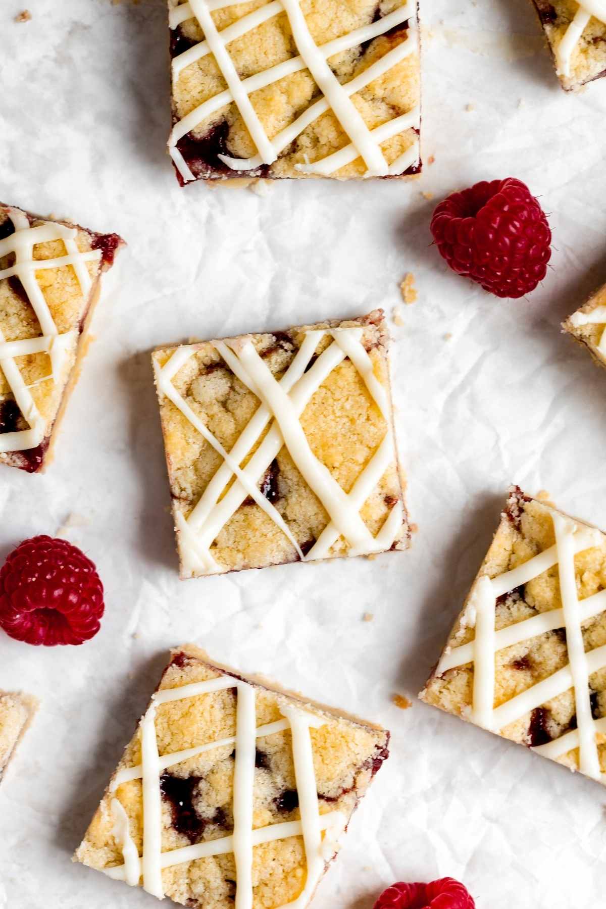 White Chocolate Raspberry Shortbread Bars sliced on parchment with fresh raspberry garnish