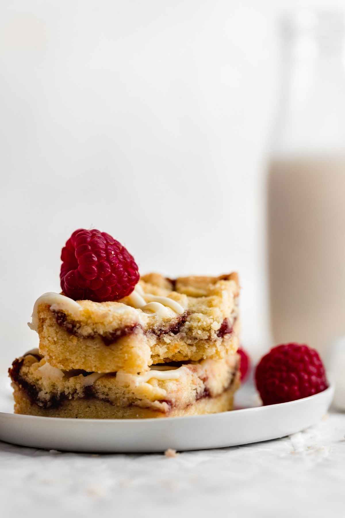 White Chocolate Raspberry Shortbread Bars sliced and stacked on a plate with fresh raspberry garnish