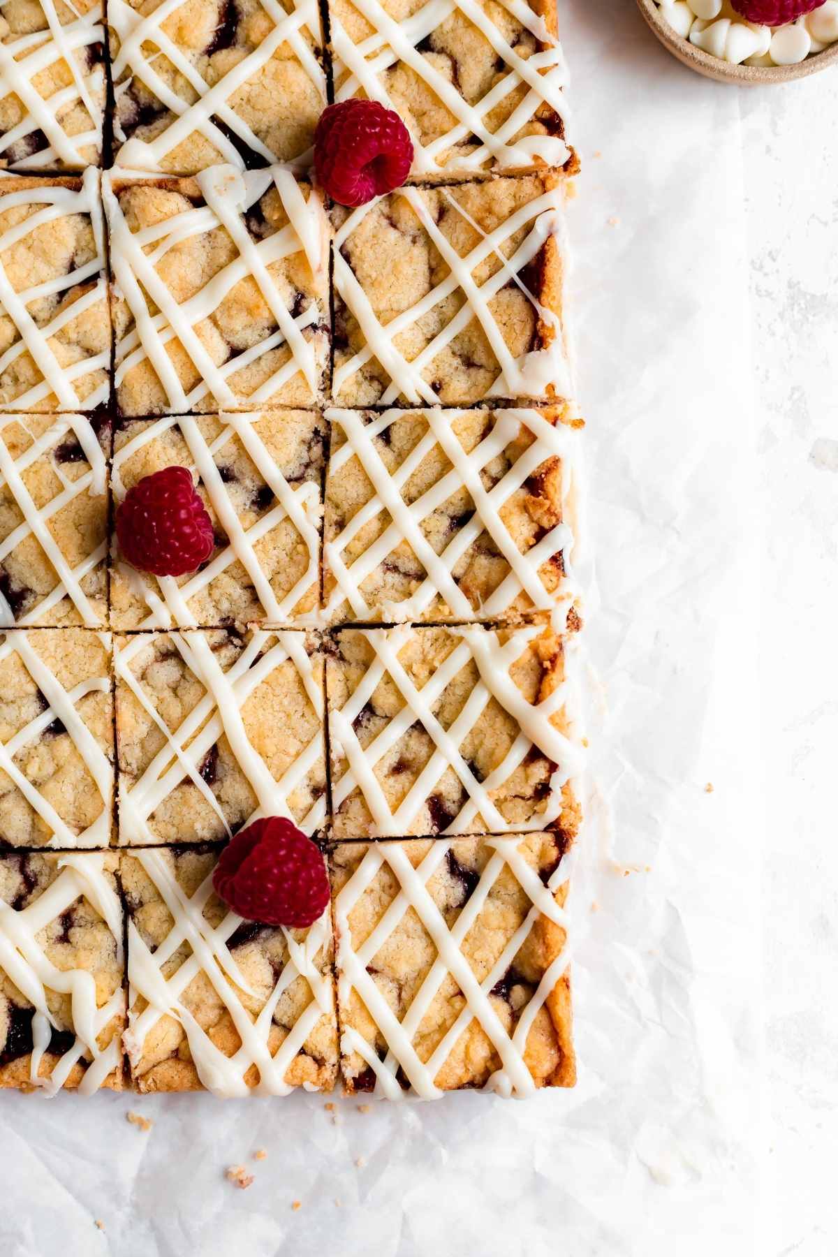 White Chocolate Raspberry Shortbread Bars sliced on parchment with fresh raspberry garnish