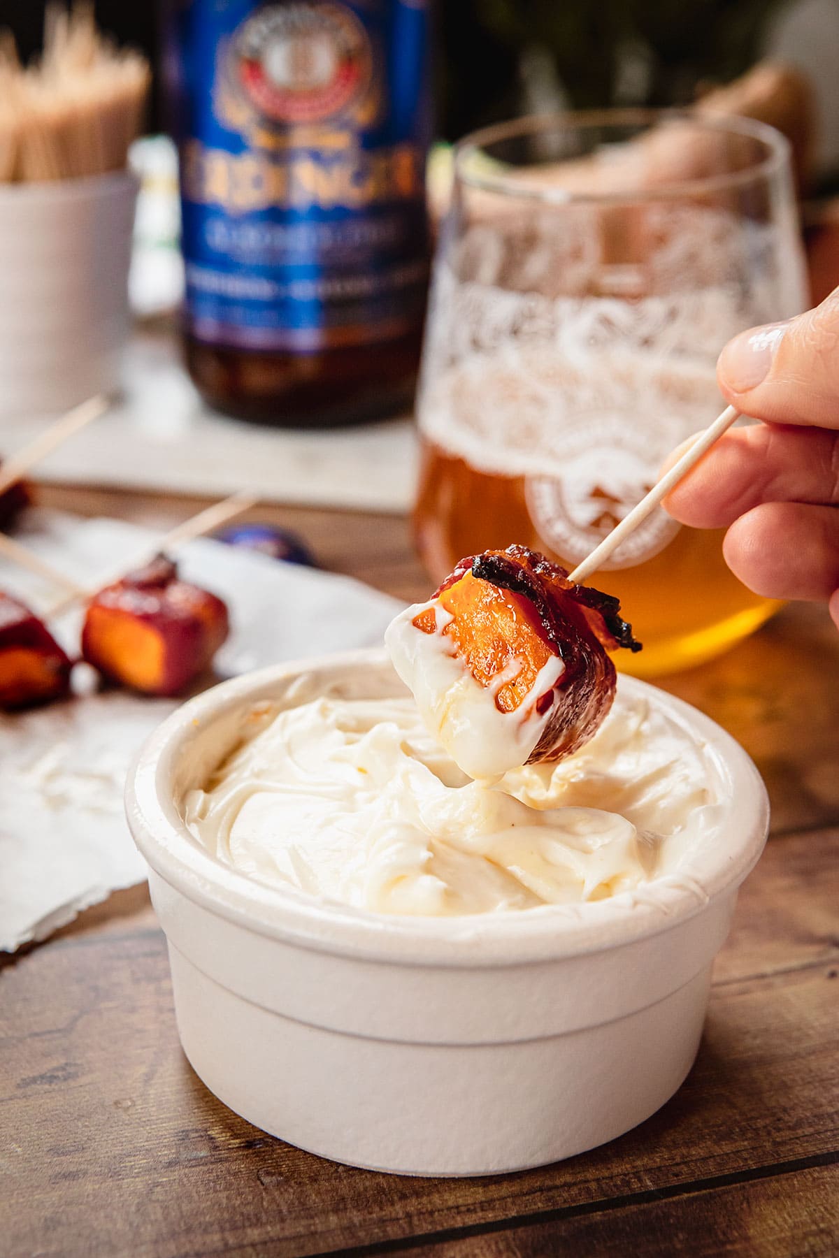 Bacon Wrapped Sweet Potatoes on toothpick being dipped in sauce