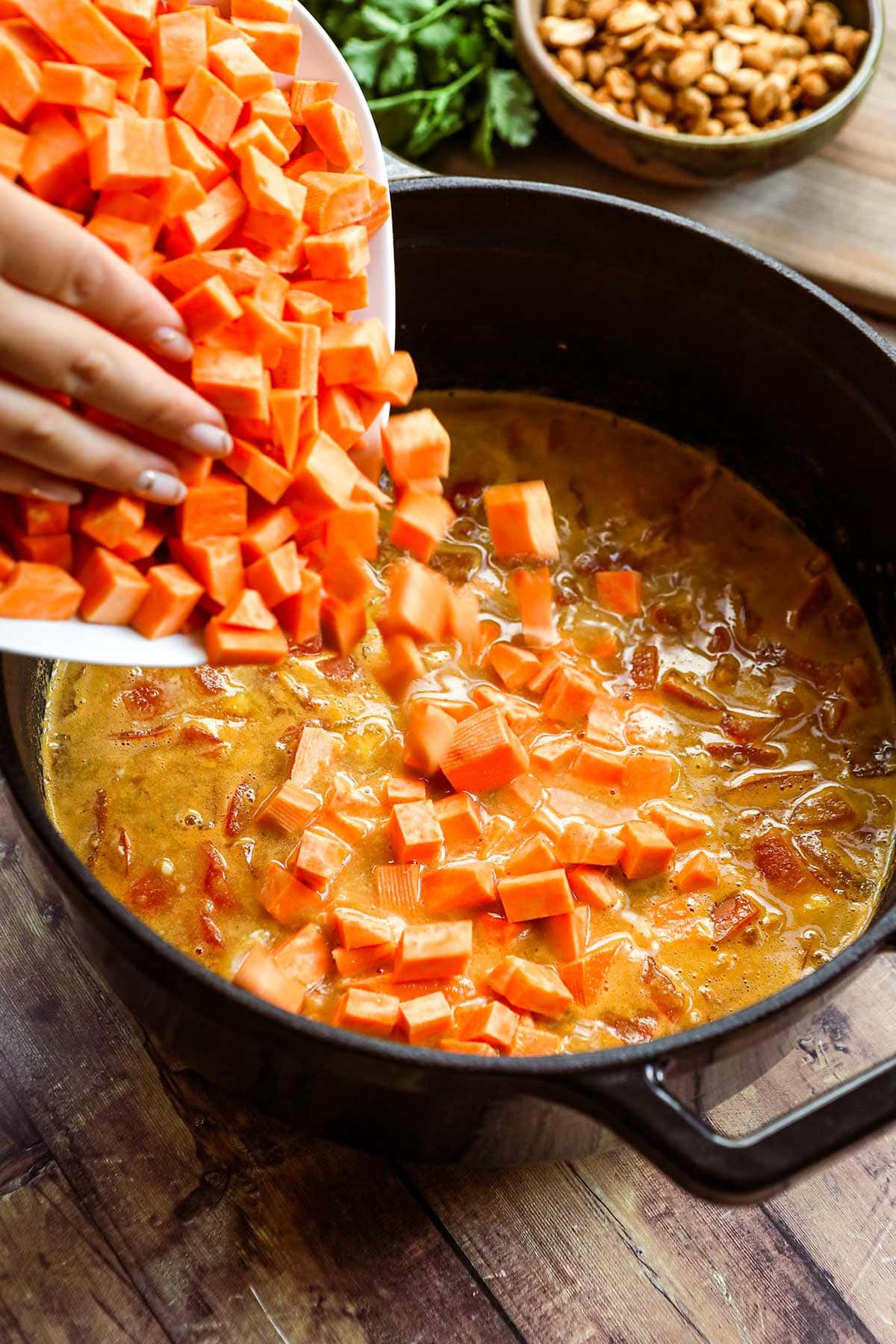 African Peanut Sweet Potato Stew in dutch oven with sweet potatoes being added