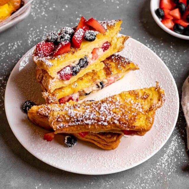 Plated halves of stuffed toast with berries and sugar