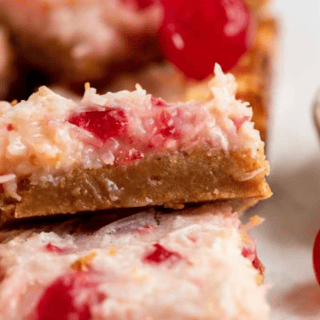 dessert squares with cherries, coconut, and cream stacked on another