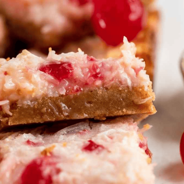 dessert squares with cherries, coconut, and cream stacked on another