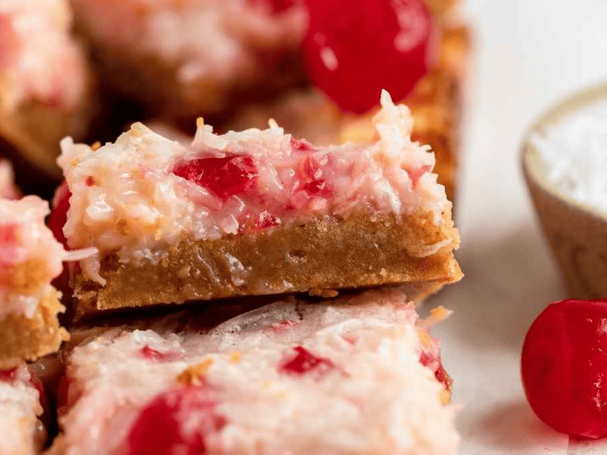 dessert squares with cherries, coconut, and cream stacked on another