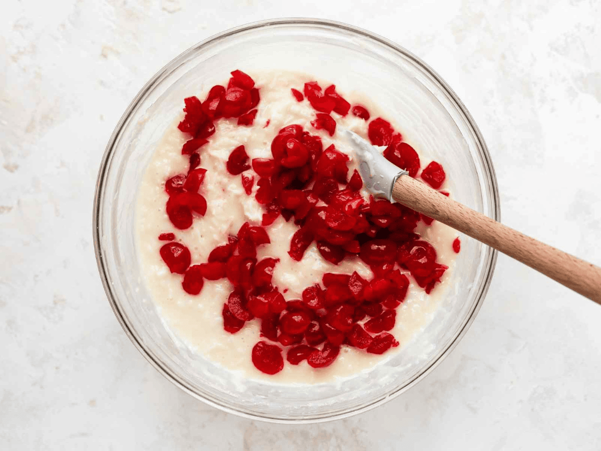 spatula in a glass mixing bowl of cream and cherries
