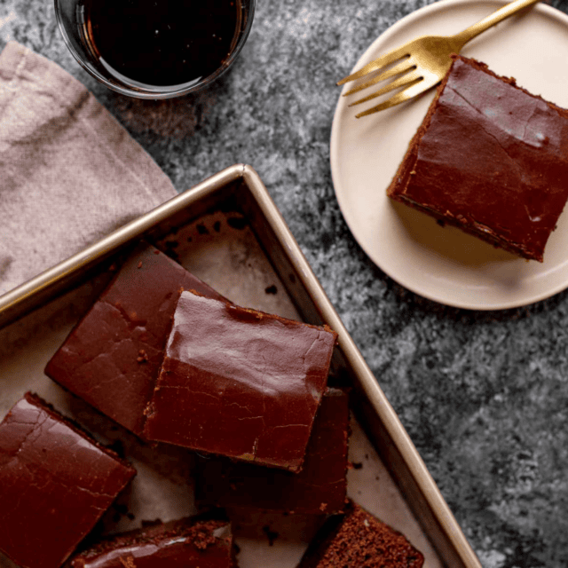 Finished caked cut into squares on a sheet pan next to a plate with a slice of cake and a gold fork.