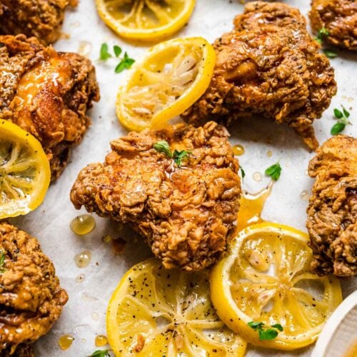 Lemon Pepper Honey Fried Chicken fried chicken pieces on parchment with lemon slices and honey drizzled