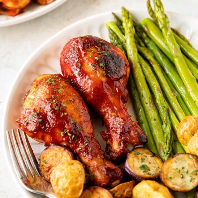 Oven Baked BBQ Drumsticks two cooked drumsticks on plate with asparagus and potatoes