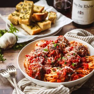 Spaghetti and Meatballs in a bowl with parmesan and parsley topping and fork