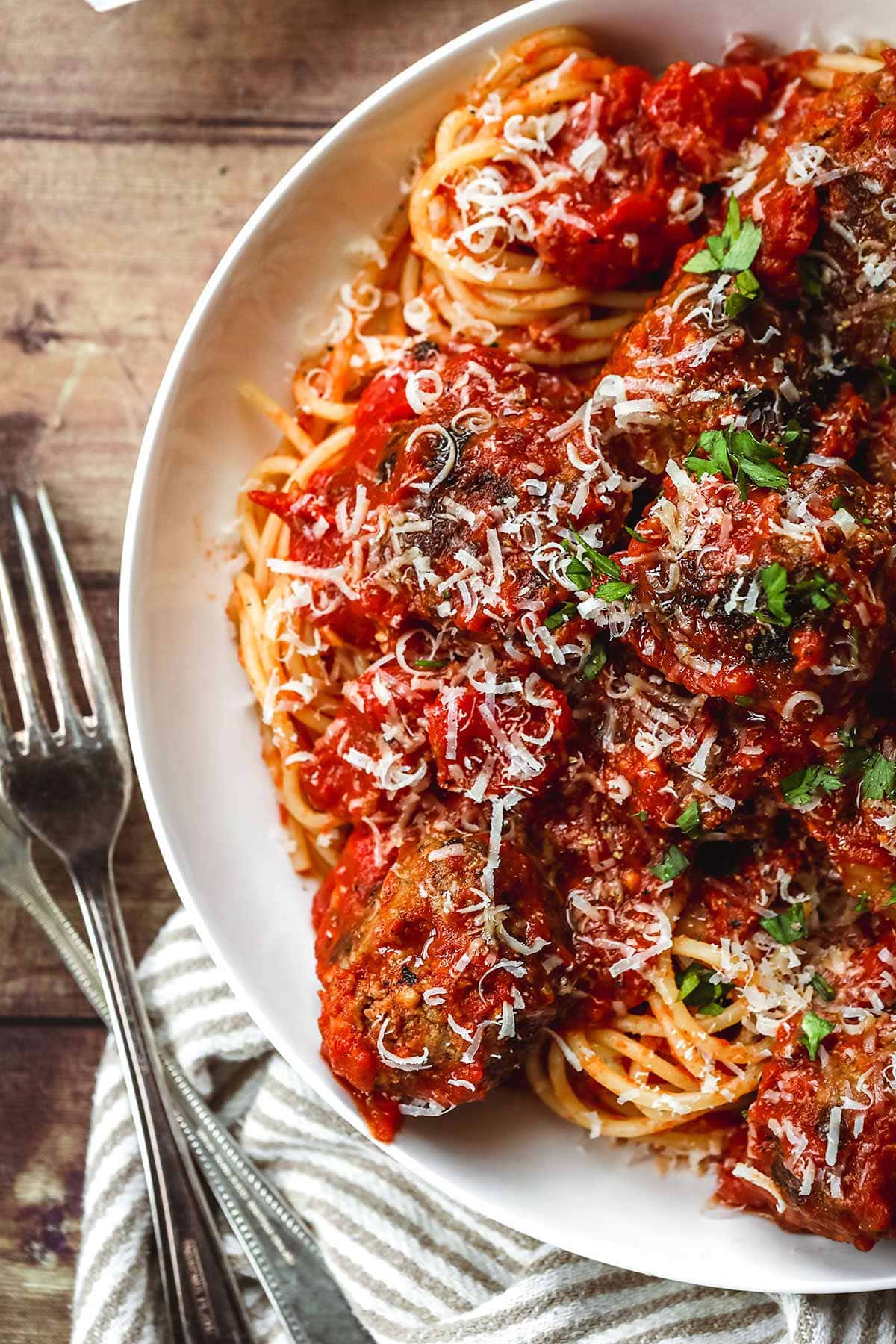 Spaghetti and Meatballs in a bowl with parmesan and parsley topping and fork