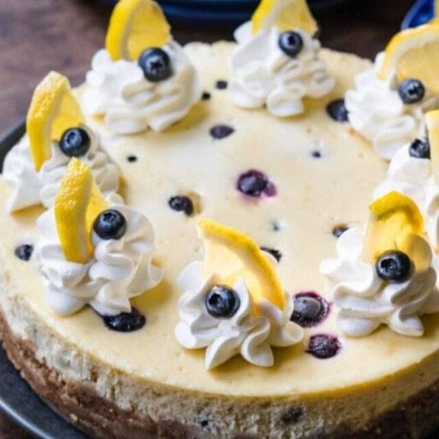 Cheesecake on serving plate with whipped cream, fresh blueberries and lemon garnish