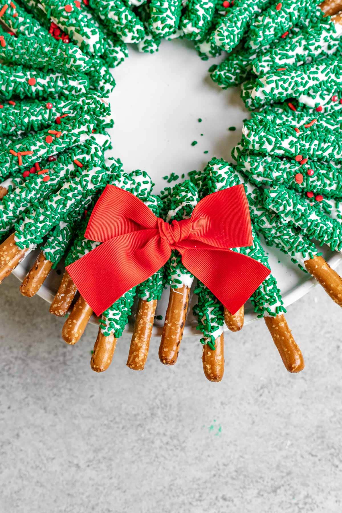 Chocolate Pretzel Wreath white chocolate coated pretzel sticks with green sanding sugar arranged as a wreath with a red bow