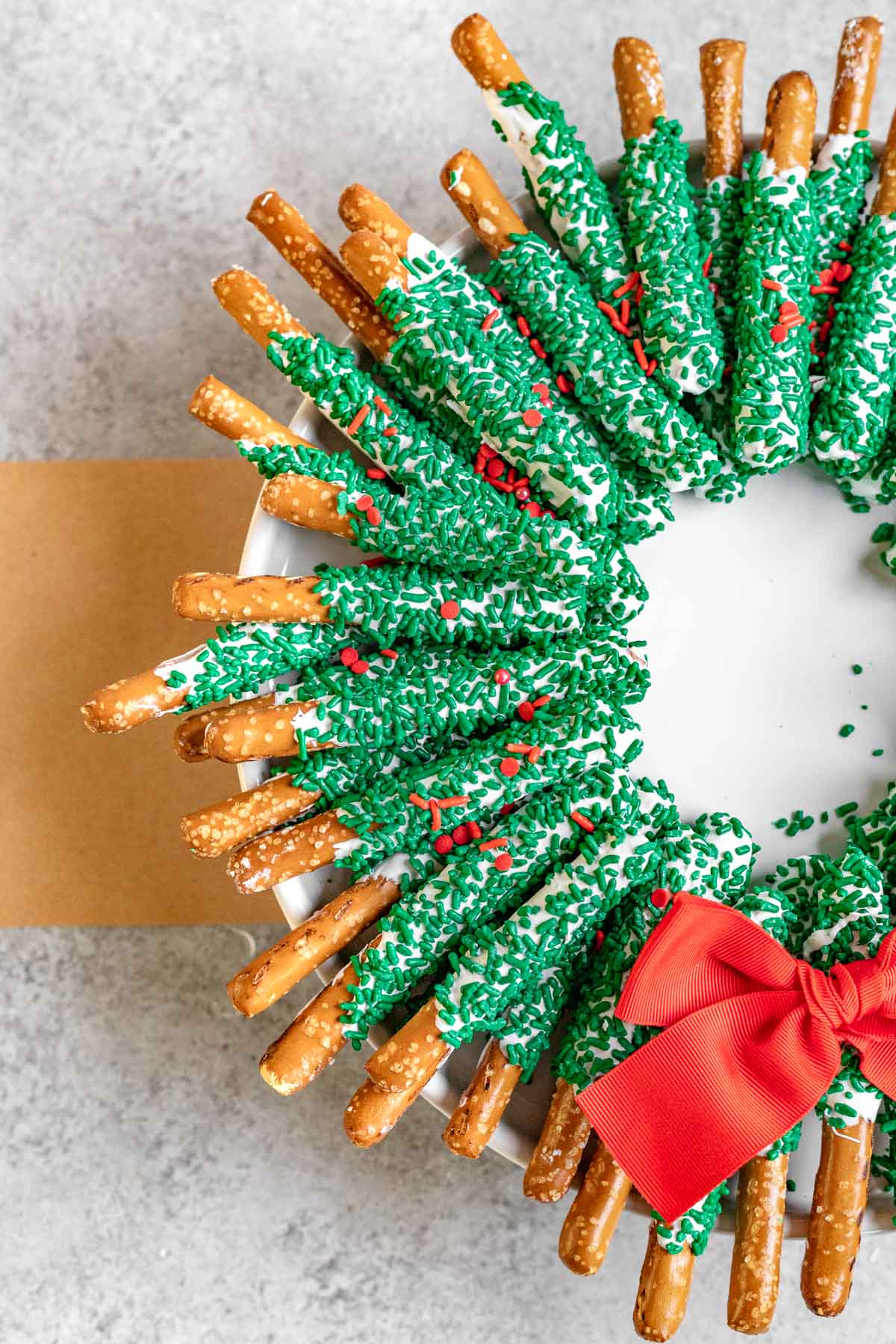 Chocolate Pretzel Wreath white chocolate coated pretzel sticks with green sanding sugar arranged as a wreath with a red bow