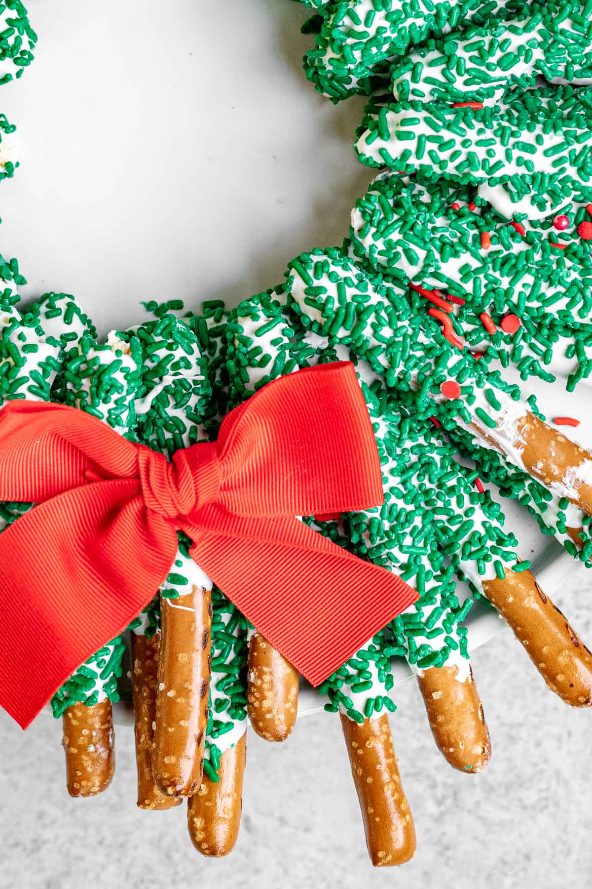 Chocolate Pretzel Wreath white chocolate coated pretzel sticks with green sanding sugar arranged as a wreath with a red bow