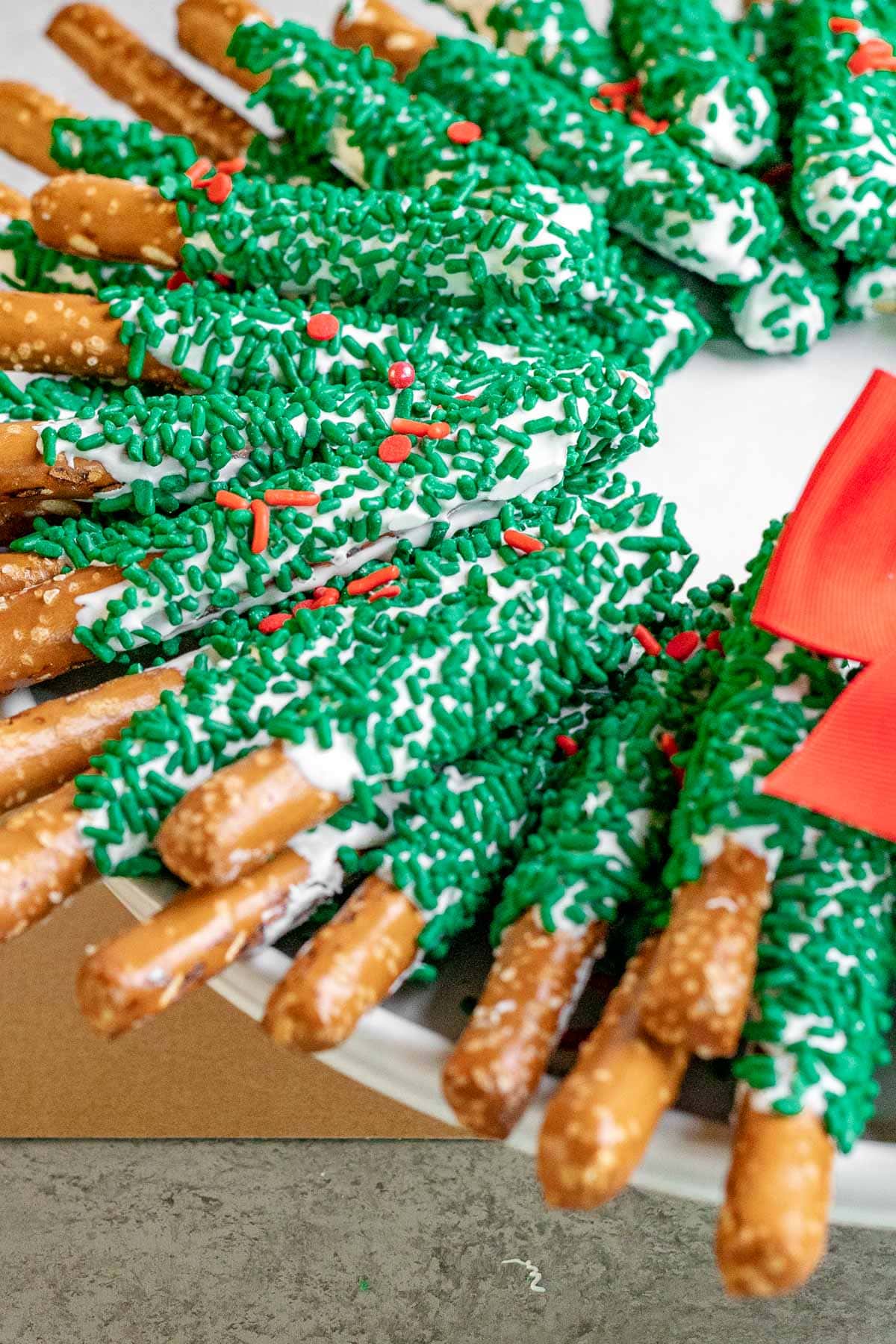 Chocolate Pretzel Wreath white chocolate coated pretzel sticks with green sanding sugar arranged as a wreath with a red bow