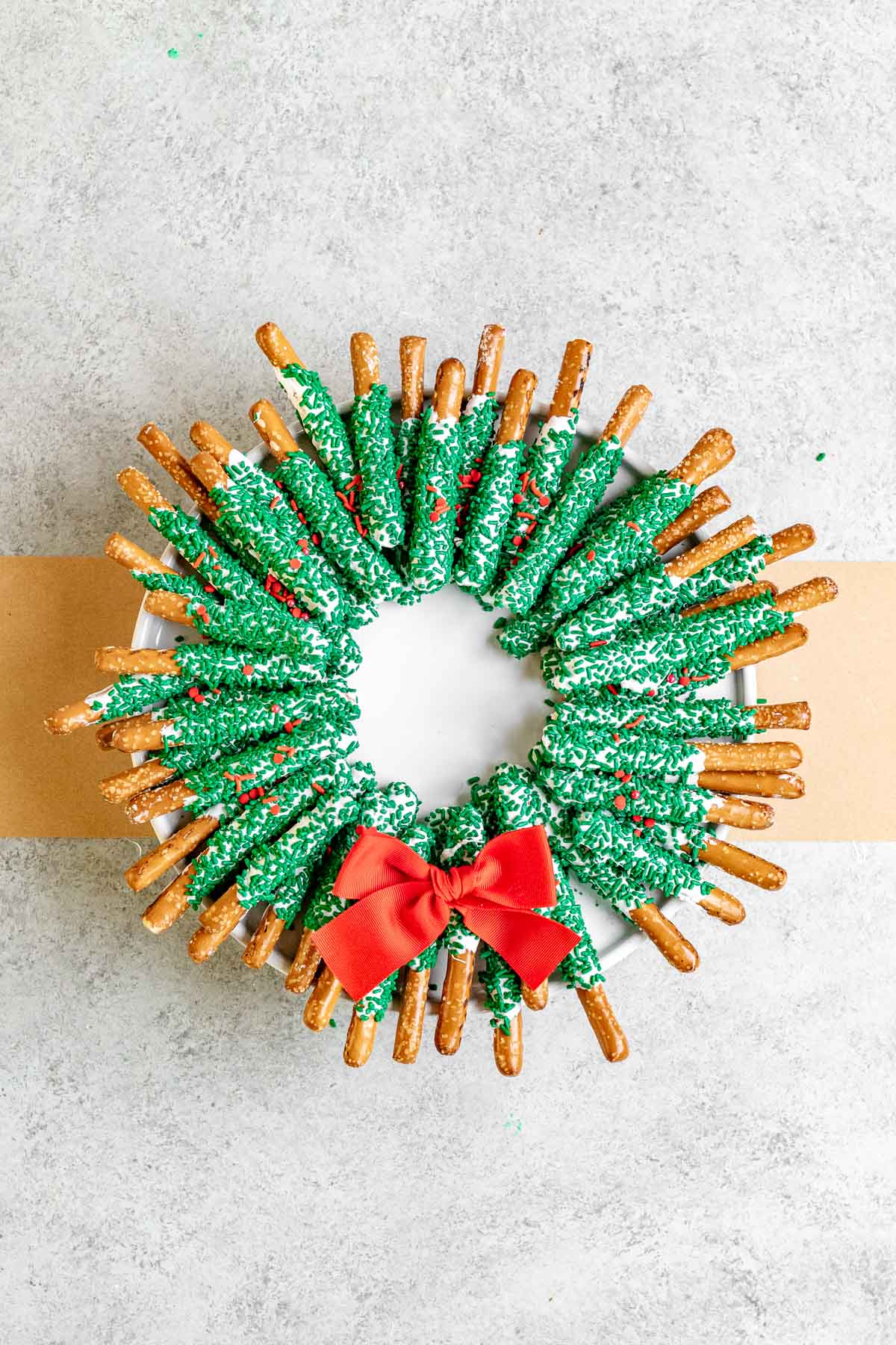 Chocolate Pretzel Wreath white chocolate coated pretzel sticks with green sanding sugar arranged as a wreath with a red bow