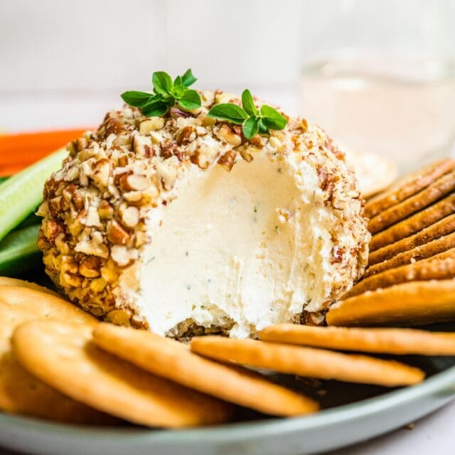 Garlic Parmesan Cheese Ball with scoop taken on serving plate with crackers and veggies