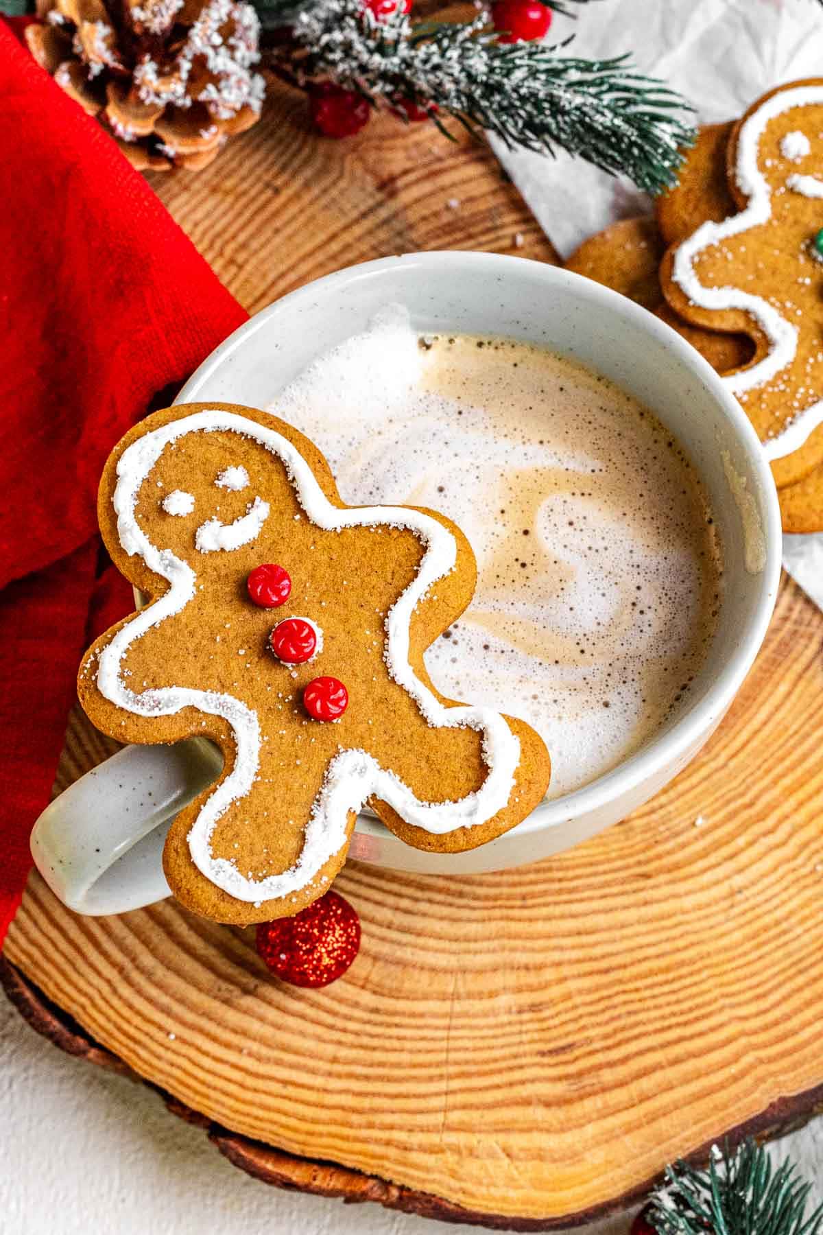 A Gingerbread Man cookie is served with a cup of hot chocolate in a white mug on a wooden serving tray.