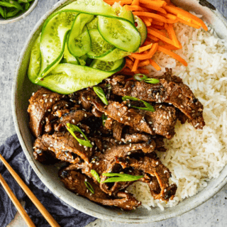 marinated beef, cucumbers, carrots, and rice in a bowl with chopsticks on the side