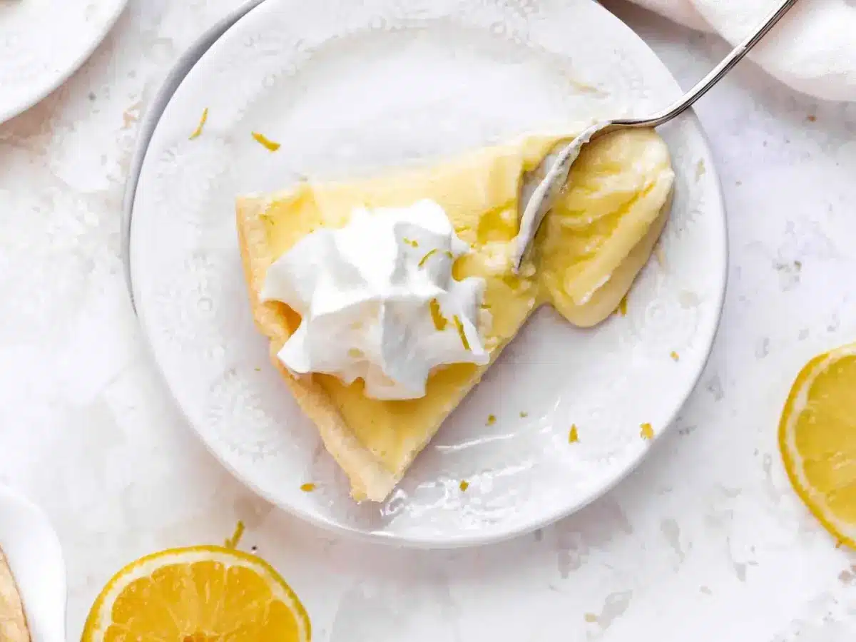 Top view of slice of yellow pie with whipped cream on top and lemons around