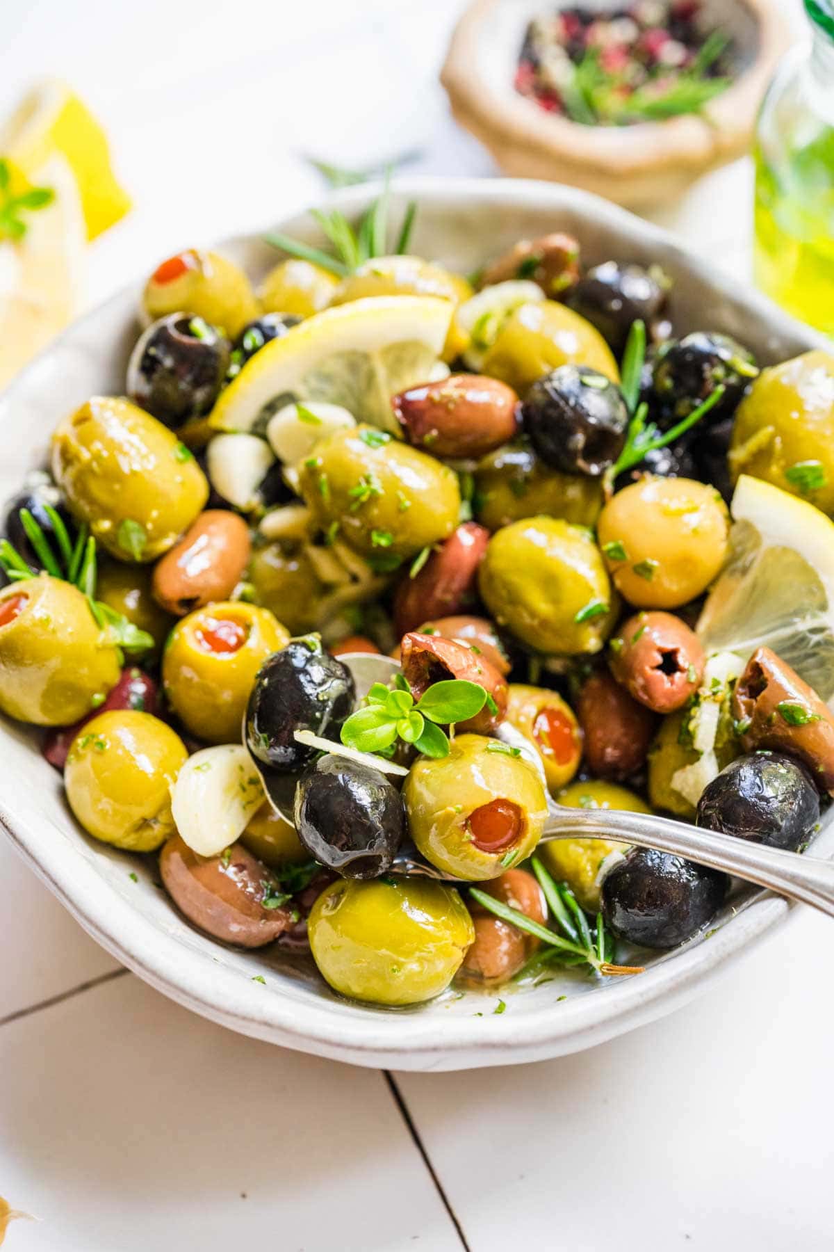 Marinated Olives olives in bowl with fresh herb and lemon garnishes and spoon