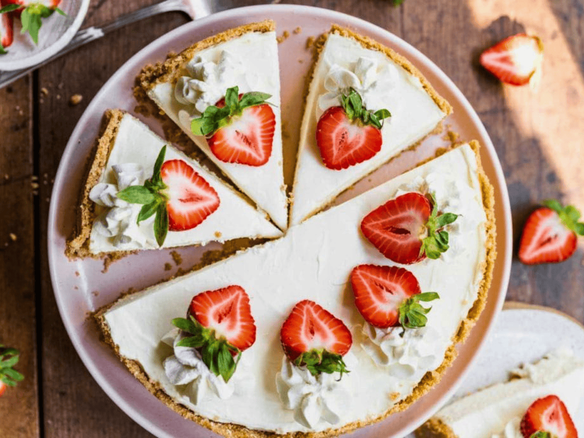 Whole cheesecake with slices cut and strawberries on top