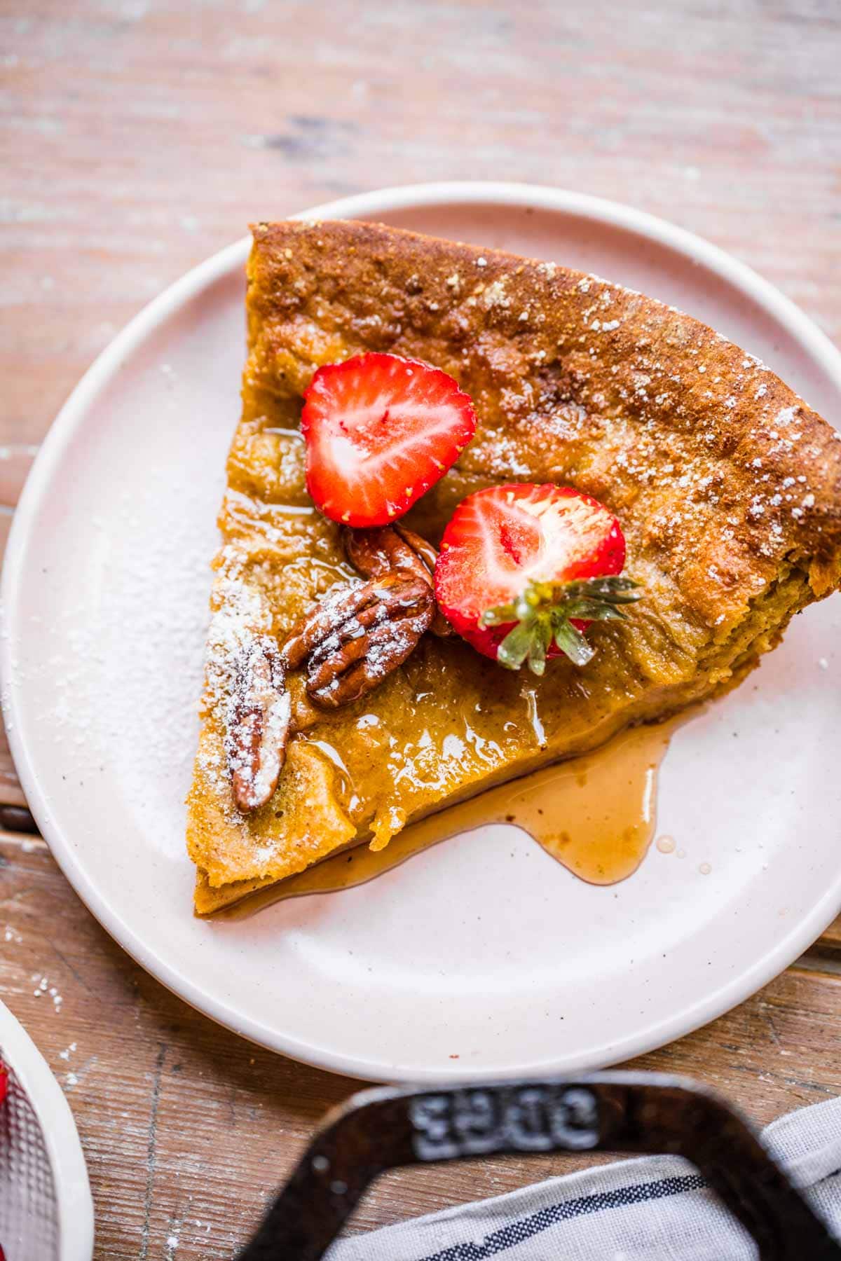 Pumpkin Dutch Baby Pancake slice on plate with strawberries and powdered sugar on top