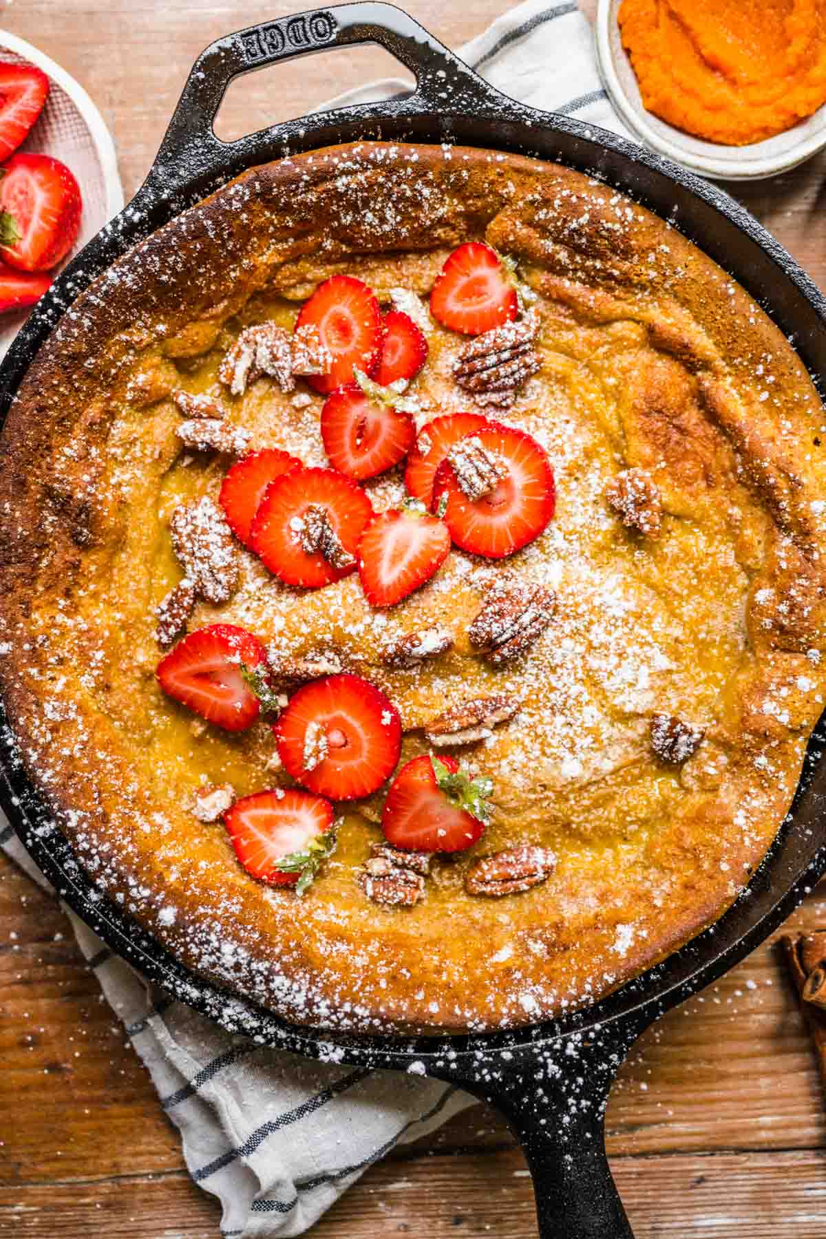 Pumpkin Dutch Baby Pancake baked in skillet with strawberries and powdered sugar on top