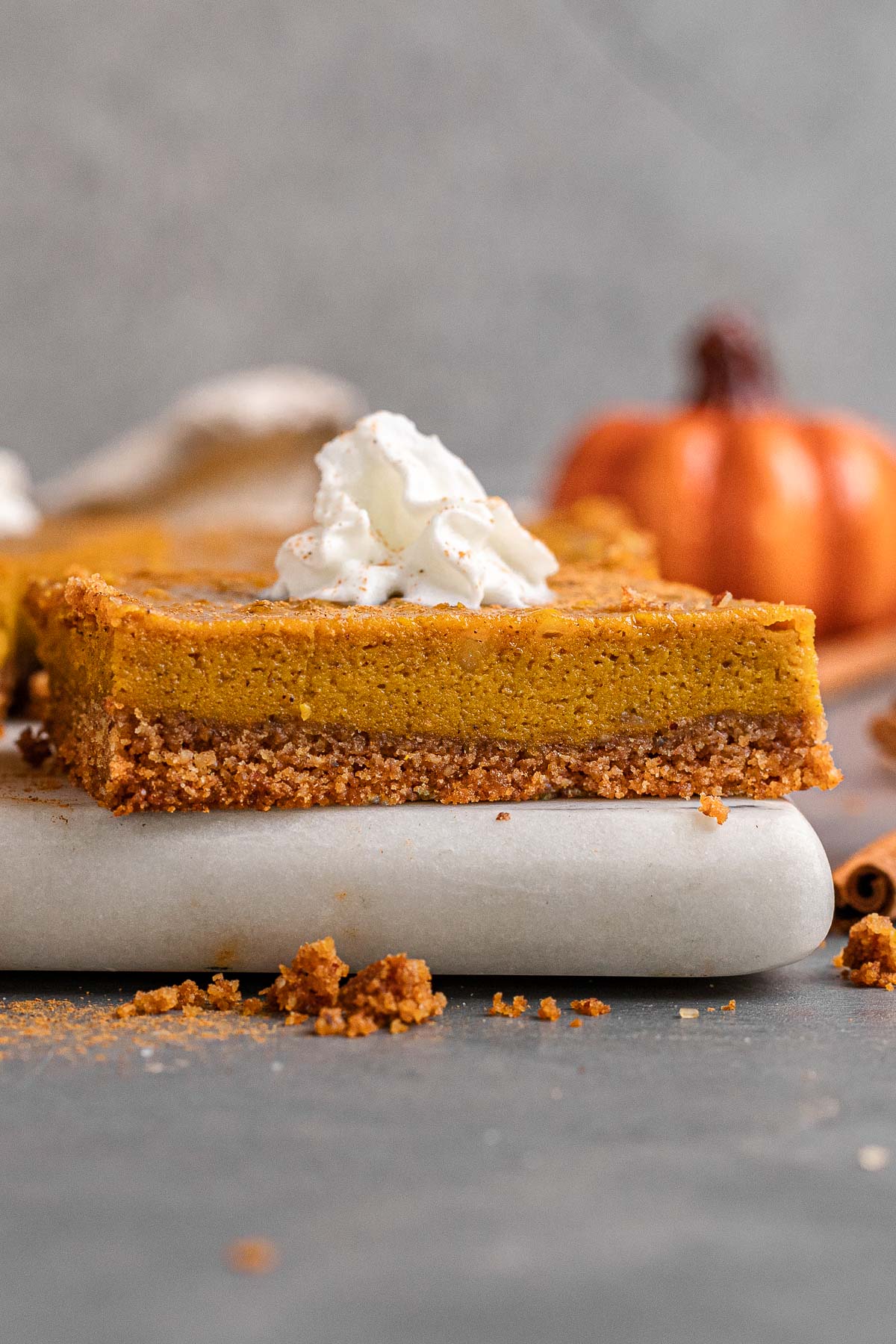 Sliced pumpkin pie bar with whipped cream. Served on a cutting board.