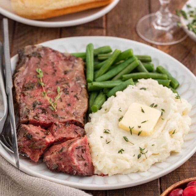 medium-rare roast slice on plate with green beans and buttered mashed potatoes