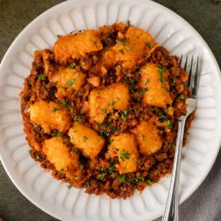 Plated casserole topped with tots with fork.