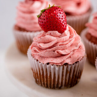 Strawberry Cupcakes frosted with strawberry on top with wrapper on plate