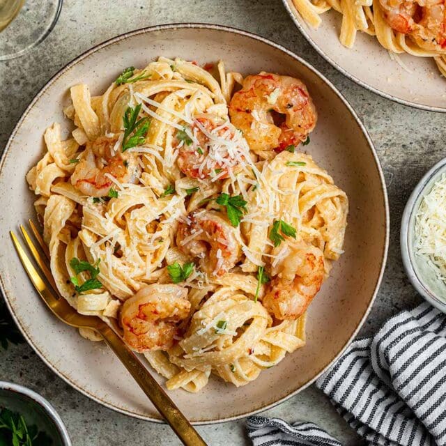 Dinner plate with pasta and shrimp tossed in sauce.