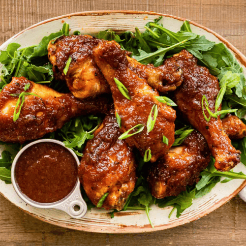 cooked sweet and spicy glazed poultry on a plate with green garnish and sauce on the side