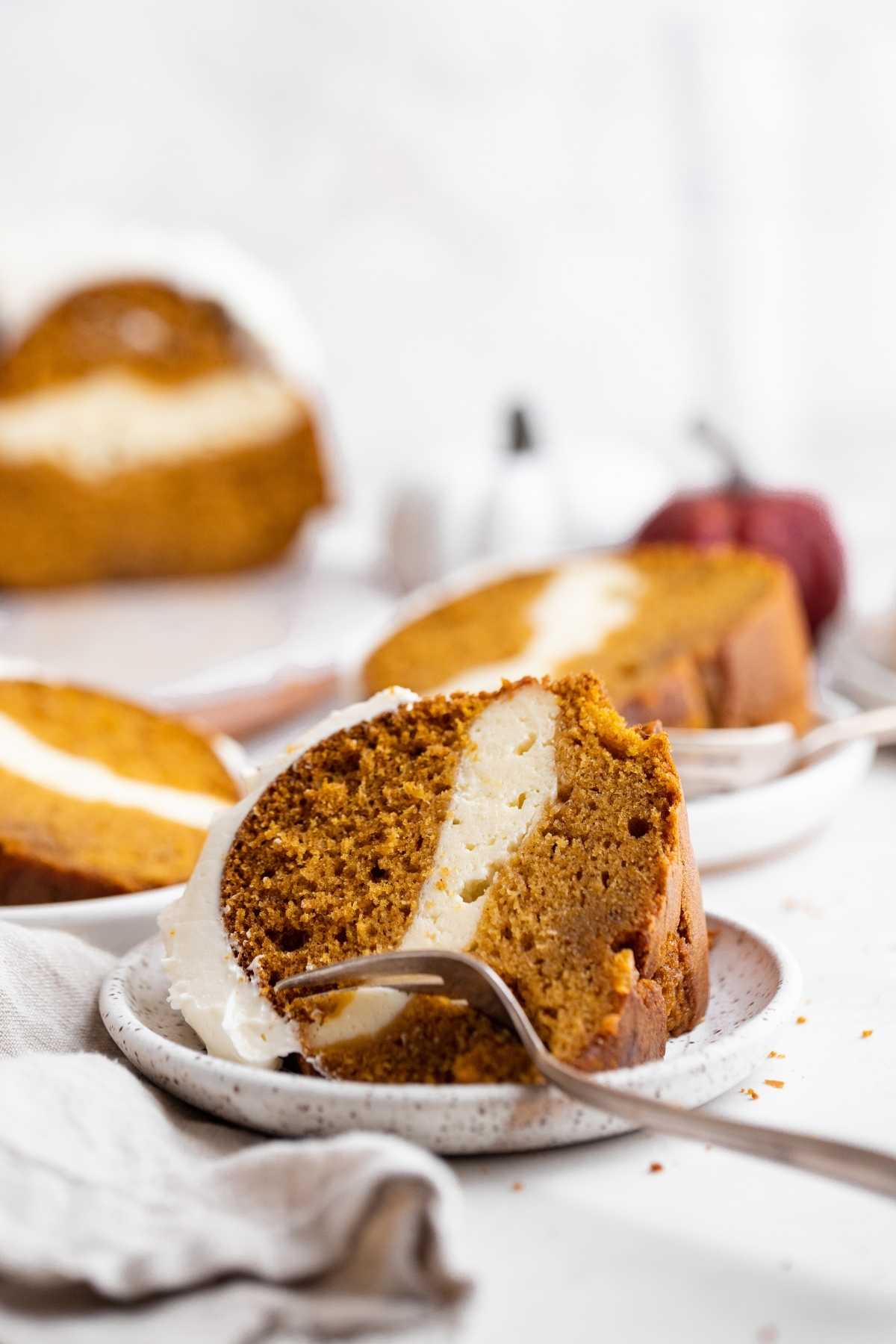 Pumpkin Cheesecake Bundt Cake slices on separate plates with fork taking bite out
