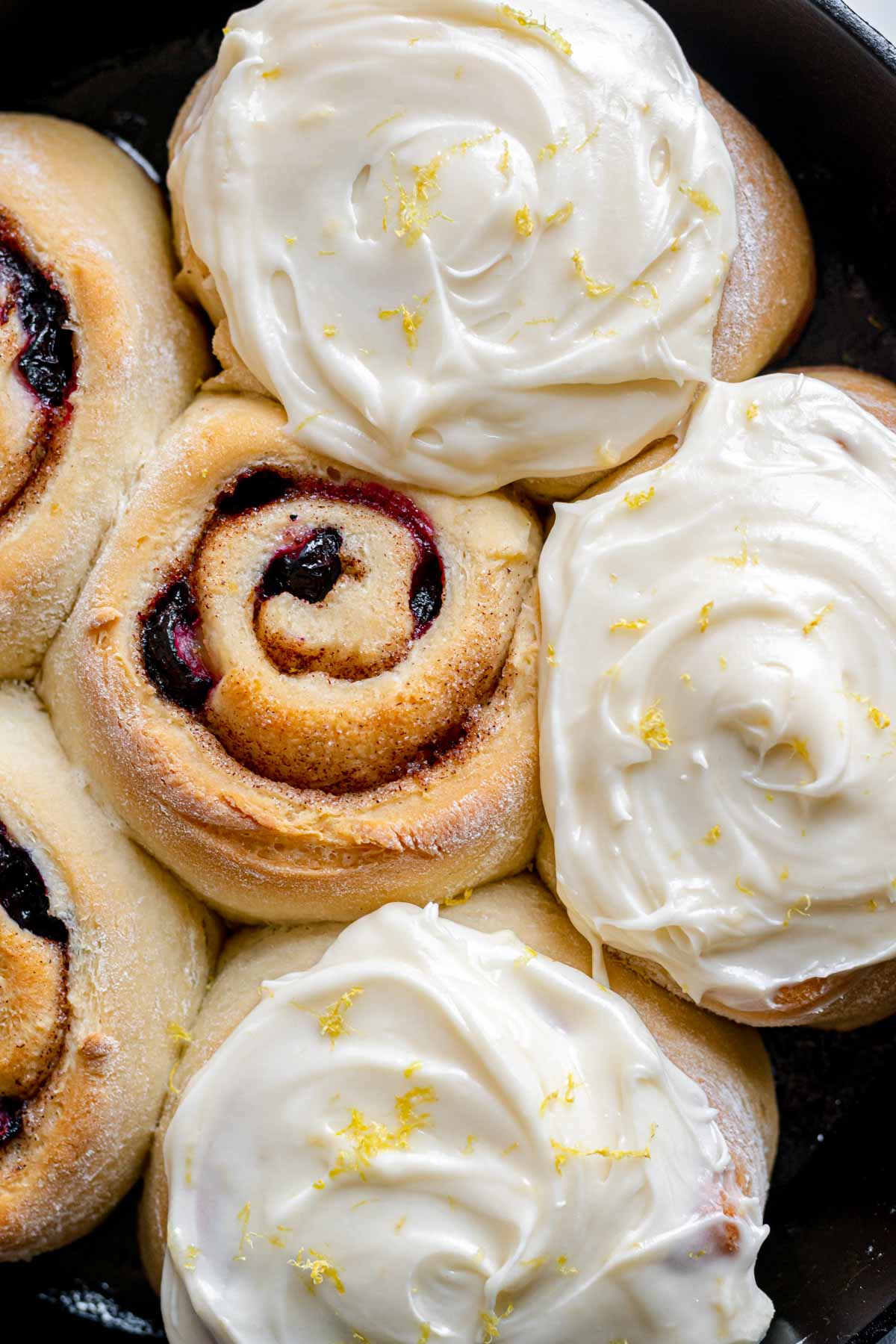 Blueberry Lemon Cinnamon Rolls baked in pan half frosted close up