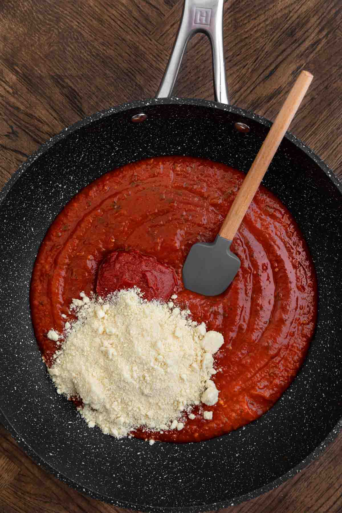 Chicken Parmesan Stuffed Peppers sauce with Parmesan cheese in skillet with spatula before stirring.