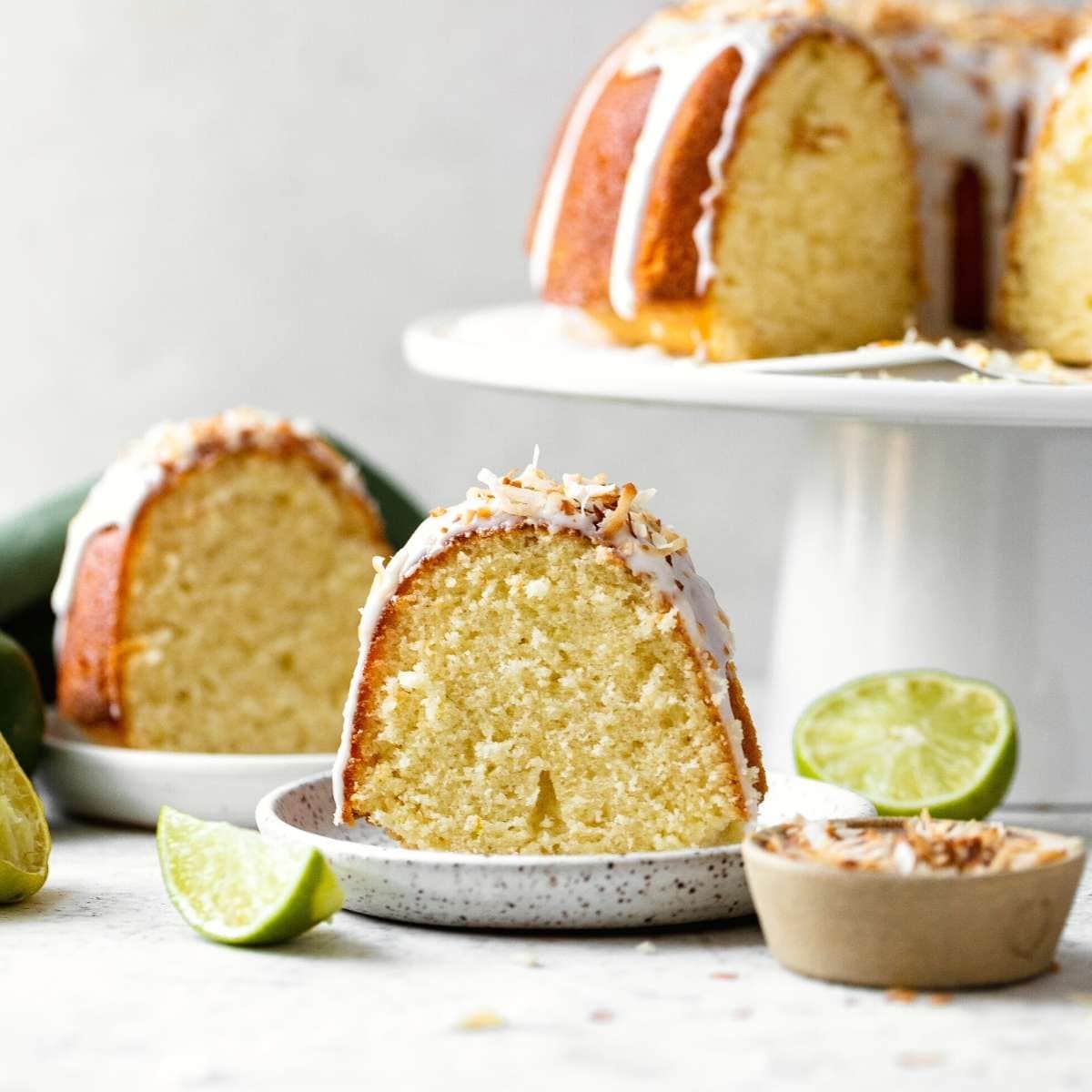 Coconut Lime Bundt Cake slice on plate with cake on stand in background