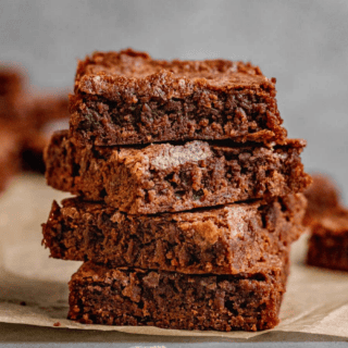 chewy chocolate dessert squares stacked on one another on parchment paper