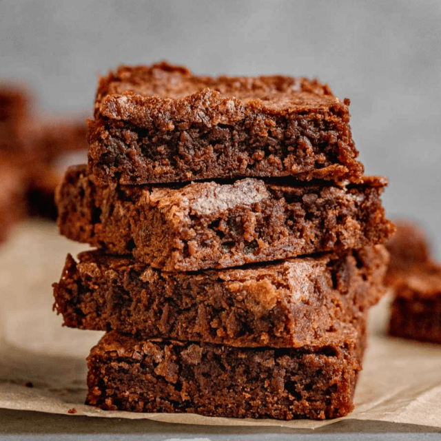 chewy chocolate dessert squares stacked on one another on parchment paper