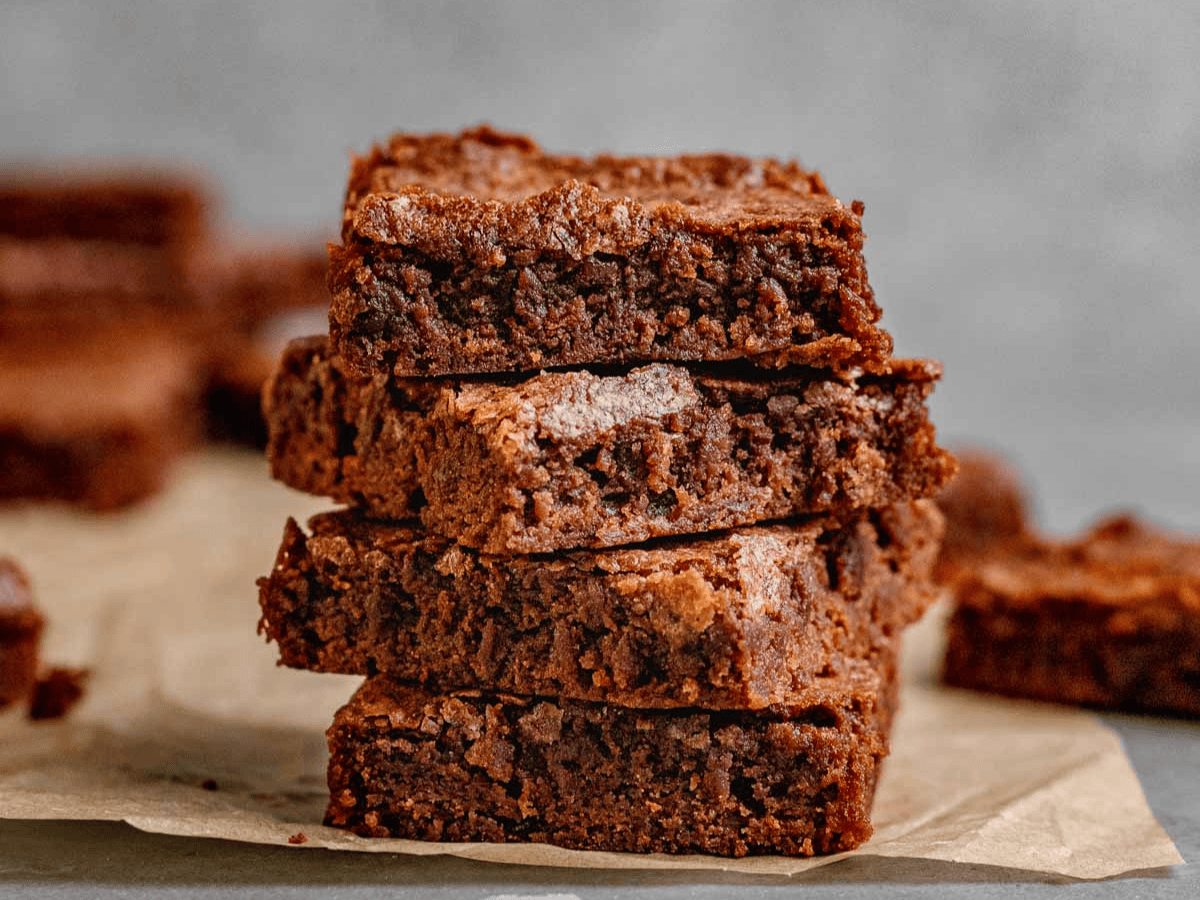 chewy chocolate dessert squares stacked on one another on parchment paper