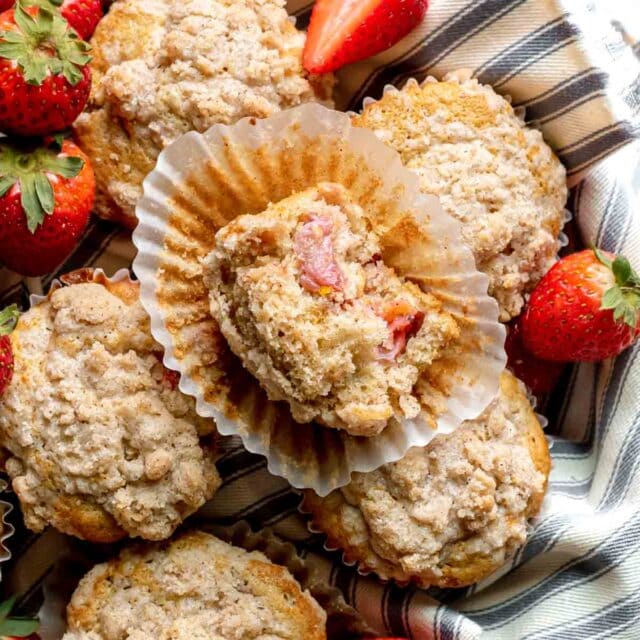 Strawberry Crumb Muffins baked in basket with wrapper pulled down and bite taken out on top muffin