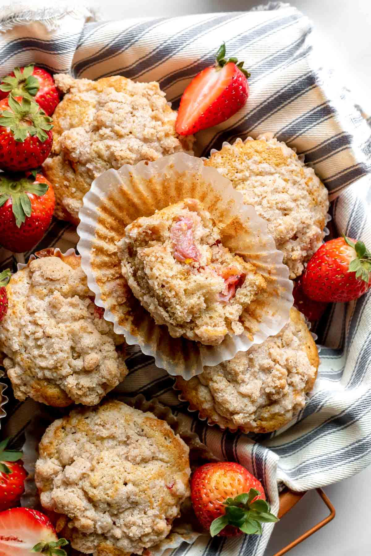 Strawberry Crumb Muffins baked in basket with wrapper pulled down and bite taken out on top muffin