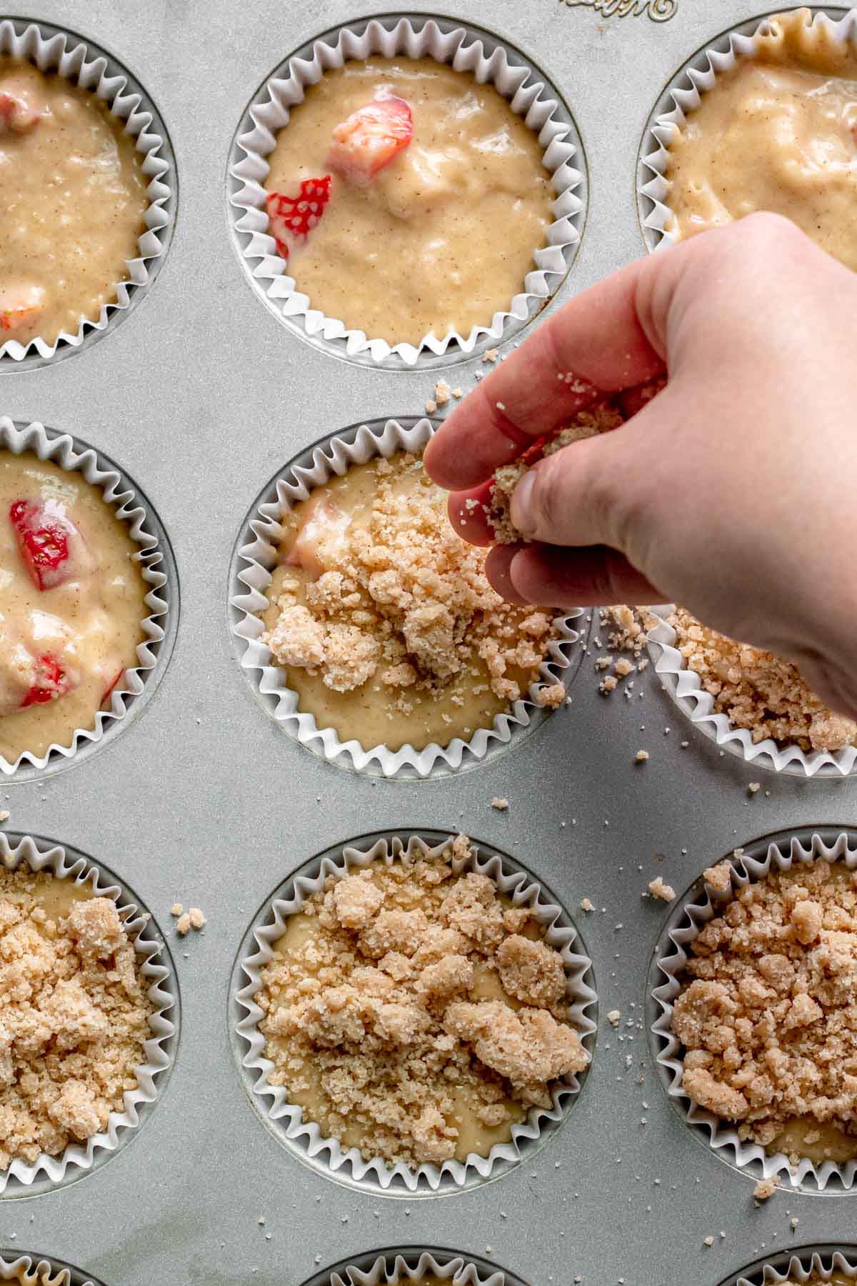 Strawberry Crumb Muffins batter in muffin tin sprinkling crumble topping