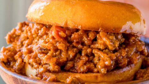Ultimate Sloppy Joes assembled sloppy Joe sandwich on wooden plate.