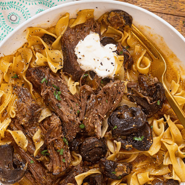 noodles, beef, sour cream, and sauce on a white plate with fork